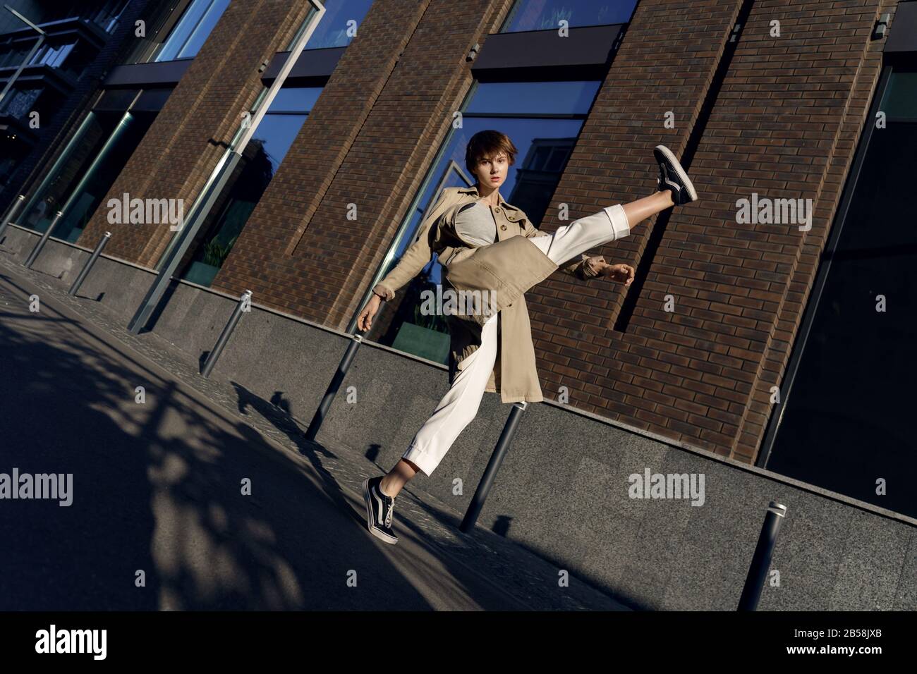 Moda ragazza indossare elegante trench posa in posa sulla strada della città guardando la macchina fotografica. Foto Stock