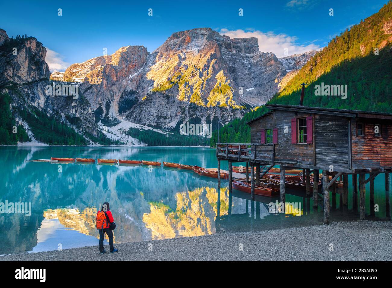 Backpacker turistico godendo della vista sulla riva del lago Braies. Luogo pittoresco con montagne innevate e barche in legno sul lago, Dolomiti, Ital Foto Stock
