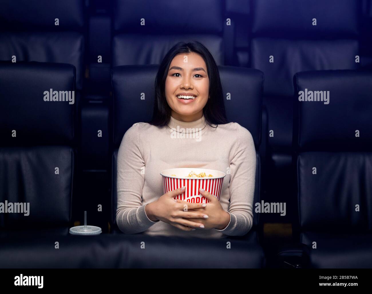 Solo nei film. Felice donna asiatica con popcorn godendo film nel cinema Foto Stock