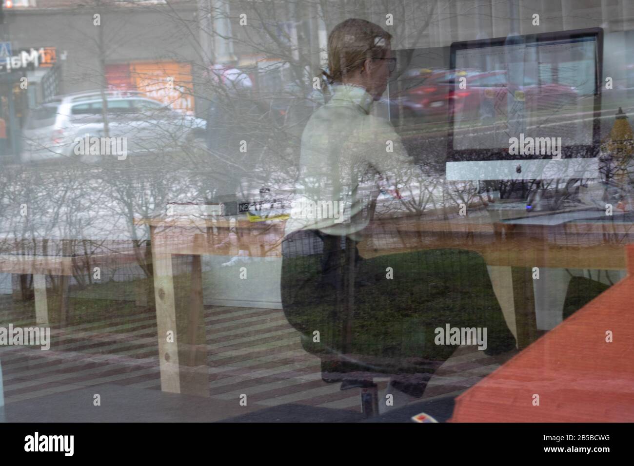 Helsinki, Finlandia - 3 marzo 2020: Donna che lavora in ufficio dietro il vetro sul laptop Mac , Editoriale Illustrativa Foto Stock