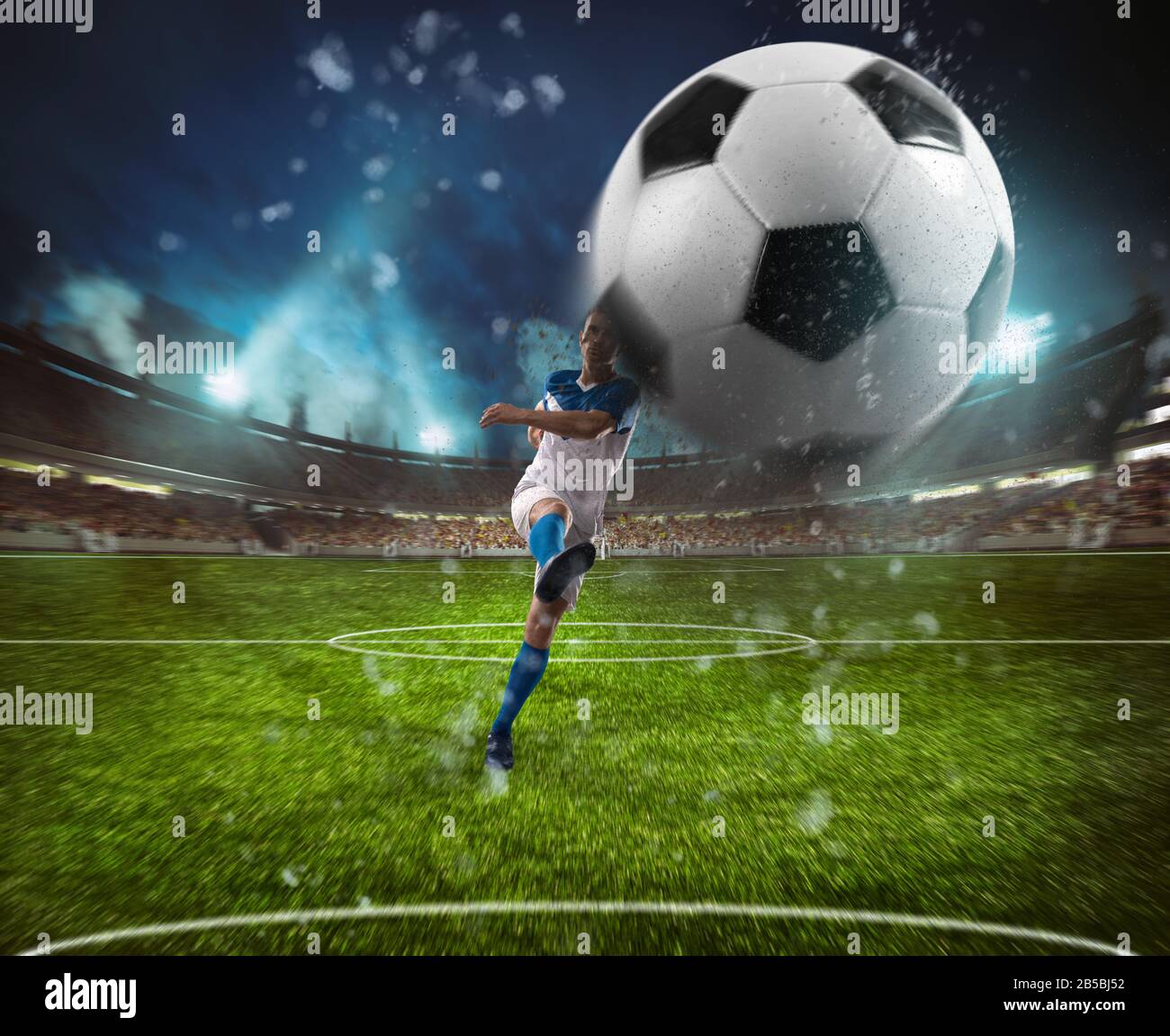 La scena calcistica di notte si abbina con il giocatore in una divisa bianca e blu che fa calciare la palla con il potere Foto Stock