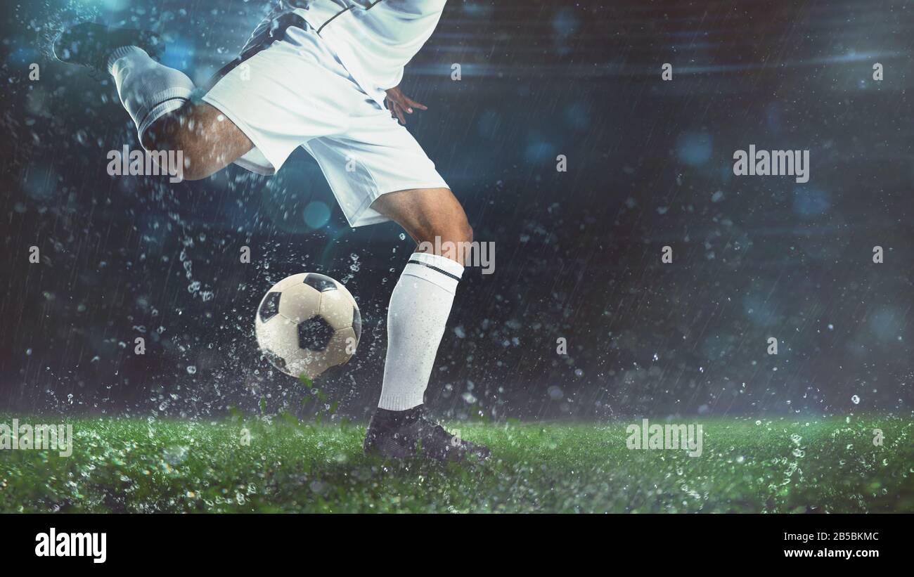 Primo piano di una scena di calcio di notte partita con il giocatore in una divisa bianca che calcia la palla con il potere Foto Stock