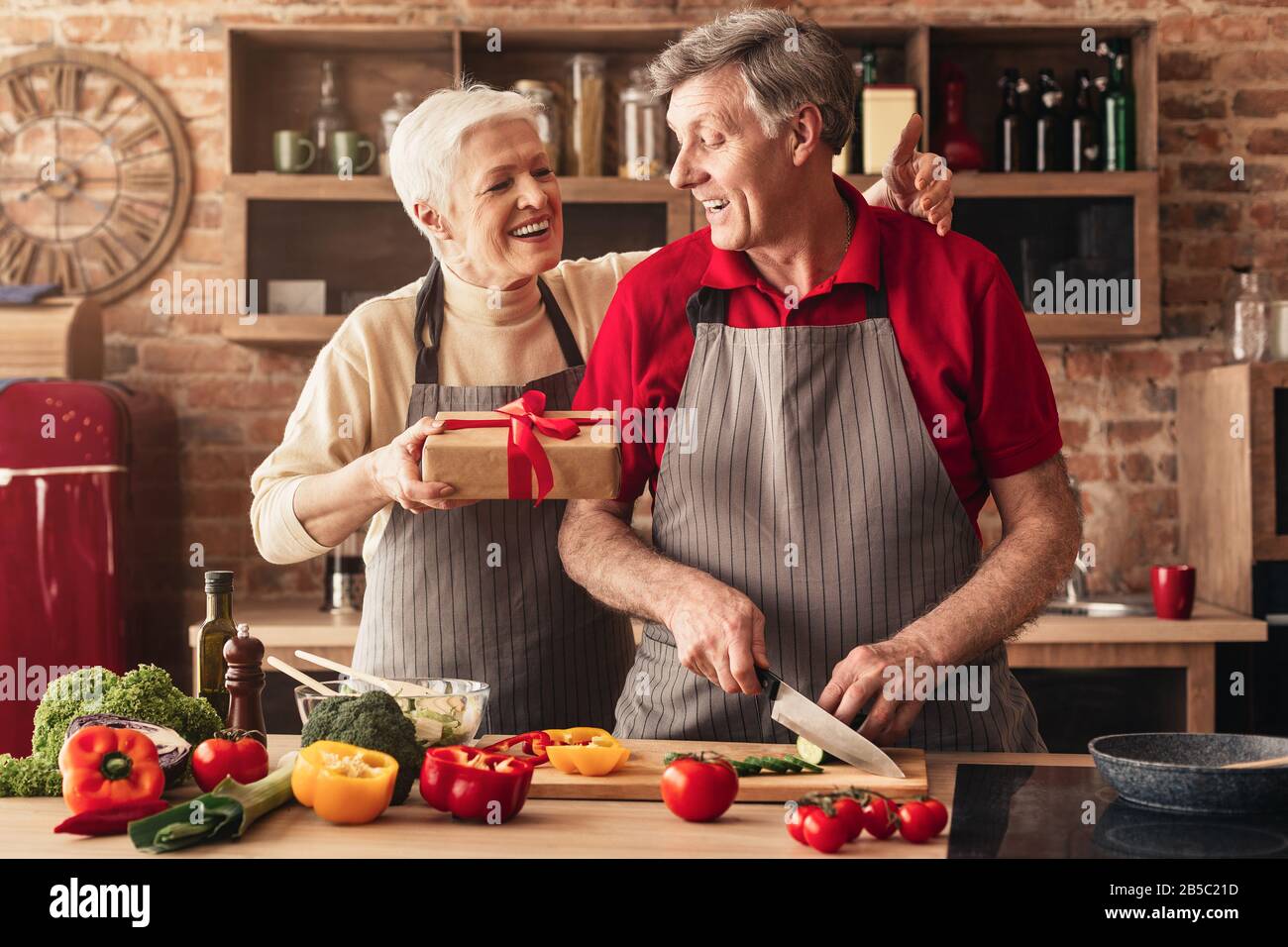 Amorevole donna anziana congratulandosi con il marito con il compleanno, dando presente in cucina Foto Stock