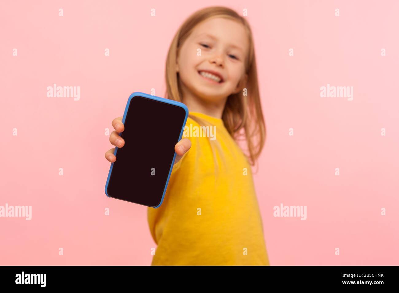 Felice sorridente preschool ragazza che tiene cellulare a fotocamera con gioiosa espressione entusiasta, pubblicità dispositivo mobile o bambini applicazione, foc Foto Stock