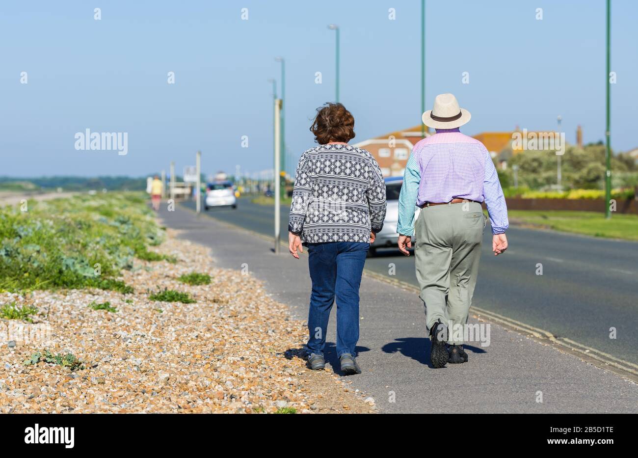 Una coppia anziana che si prende una passeggiata mattutina lungo una strada di fronte al mare in estate nel Regno Unito. Foto Stock