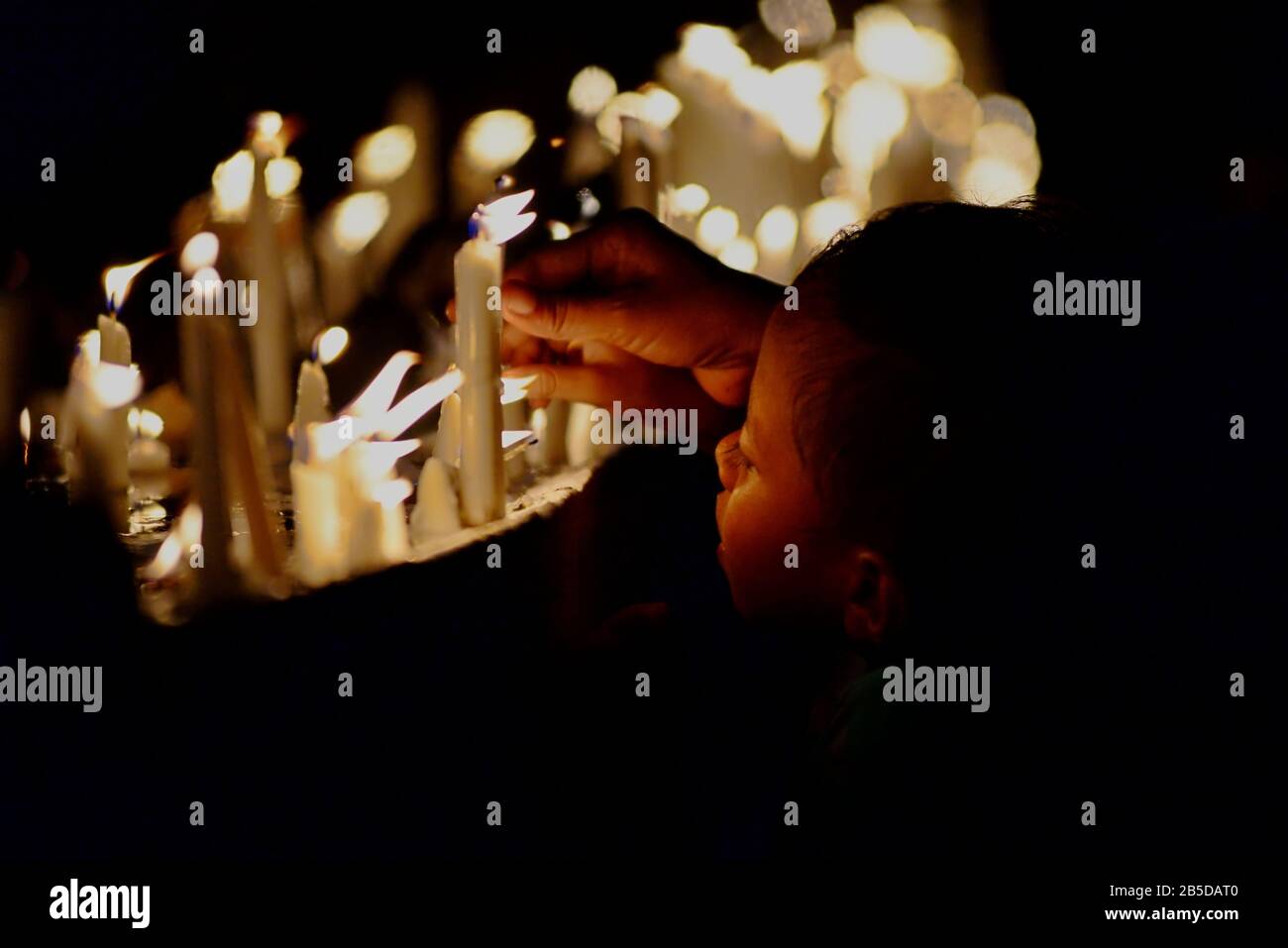 Un ragazzo non identificato accompagna i suoi genitori, illuminando le candele prima di una preghiera al cimitero della Cattedrale di Larantuka, una parte della Commemorazione del Venerdì Santo. Foto Stock