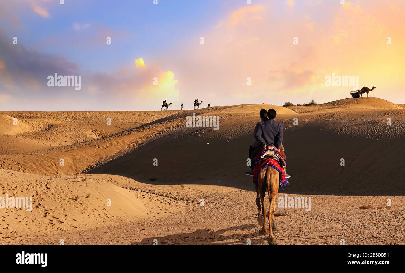 Coppia turistica godere di un safari del cammello al tramonto al deserto di Thar Jaisalmer Rajasthan, India Foto Stock