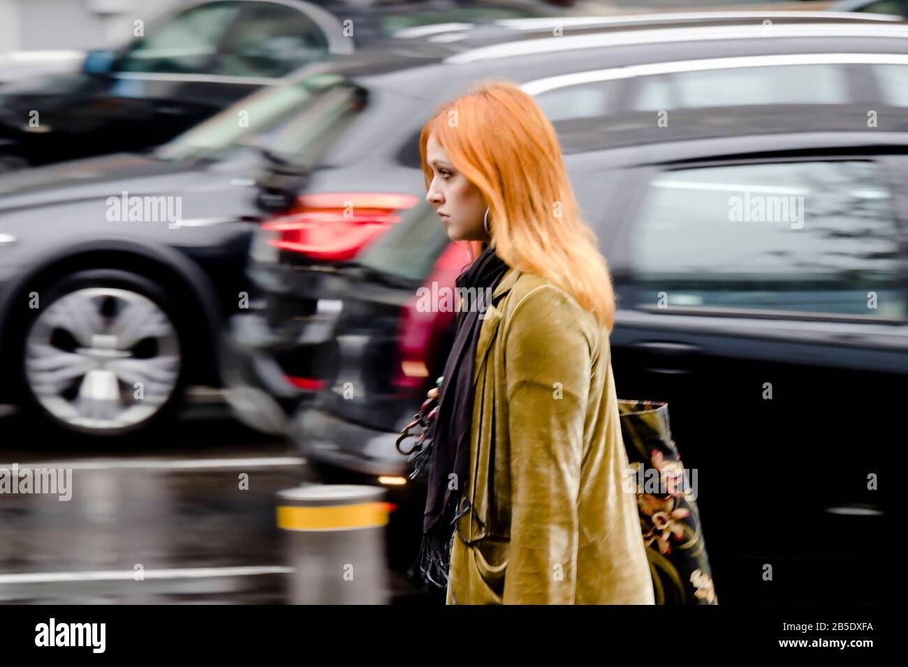 Belgrado, Serbia - 24 settembre 2019 : giovane bella donna redhead camminare da sola sulla strada piovosa della città in movimento sfocatura, e auto in movimento dietro di lui Foto Stock