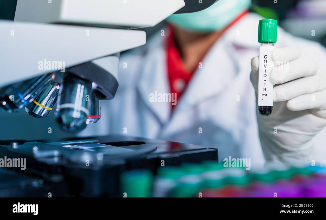 Microbiologo con una provetta di campione biologico contaminata da Coronavirus con etichetta Covid-19 / medico in laboratorio con una provetta biologica per Foto Stock