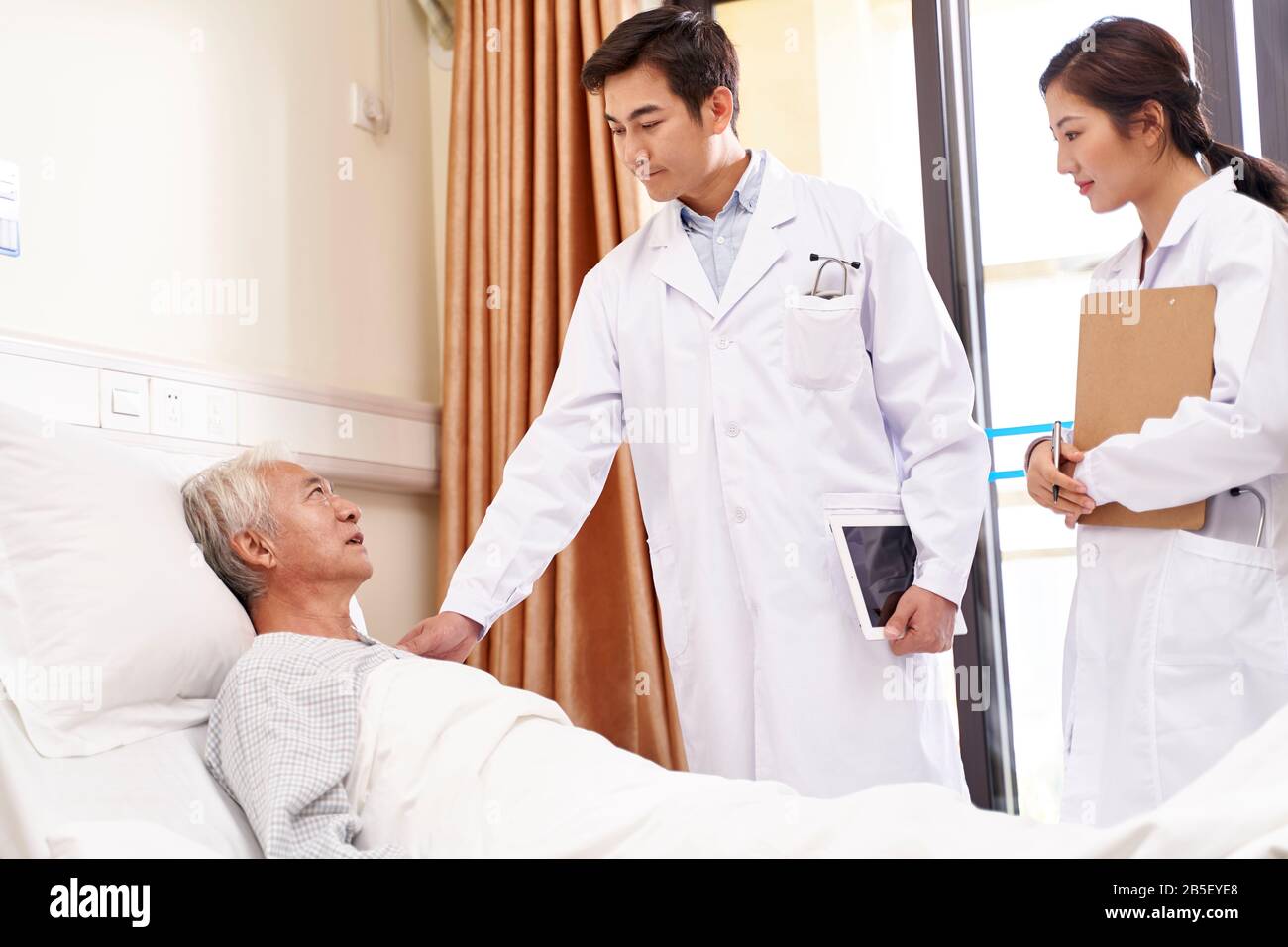 uomo asiatico anziano maschio sdraiato a letto parlando con i medici in reparto ospedaliero Foto Stock