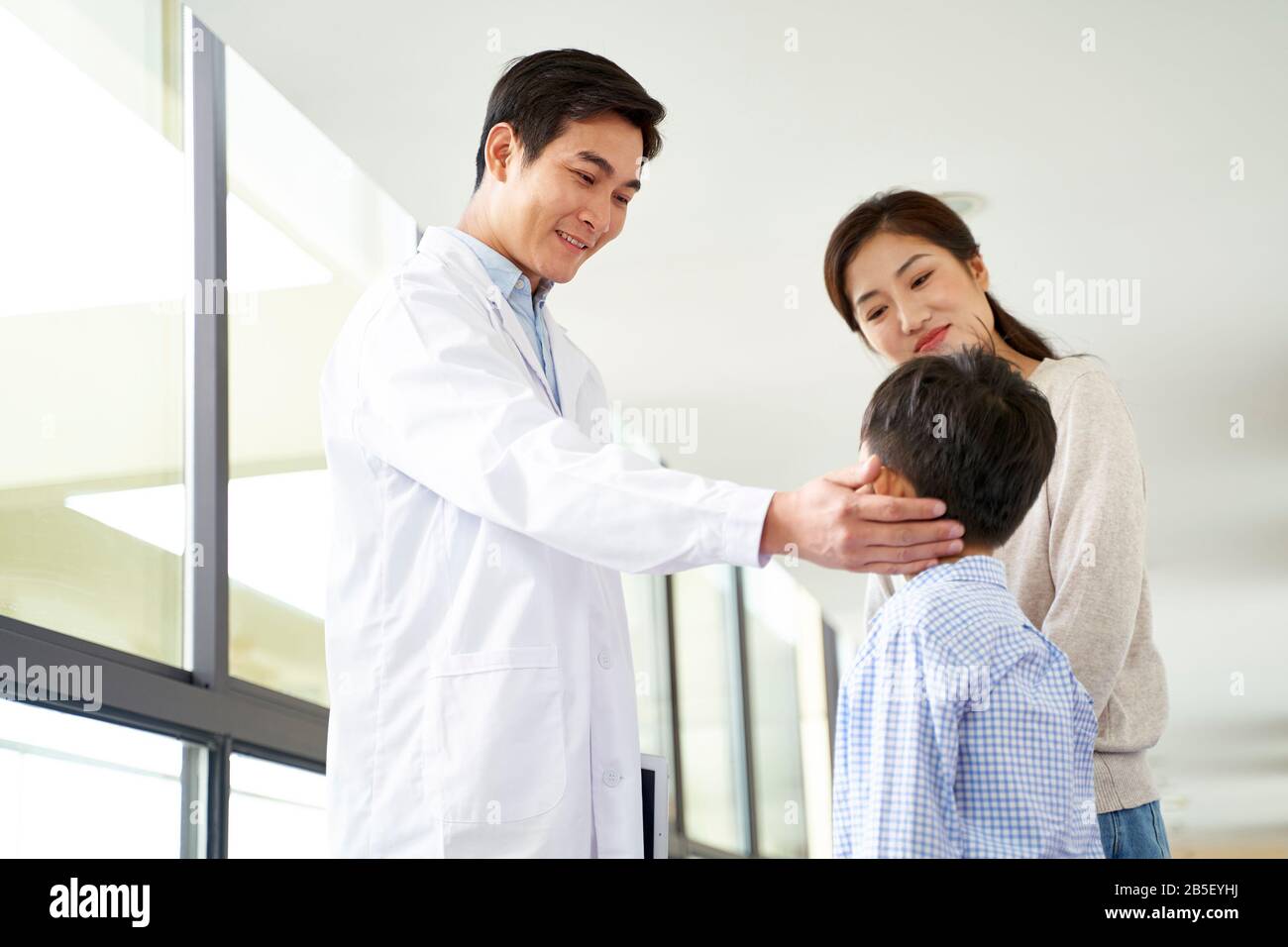 amichevole giovane medico di pediatria asiatica che parla con madre e figlio nel corridoio dell'ospedale Foto Stock