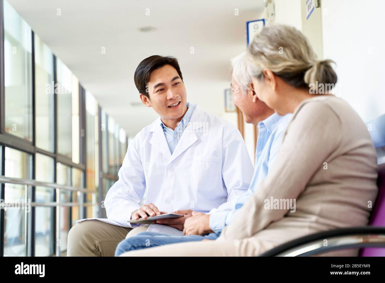 un giovane medico asiatico cordiale che parla con la vecchia coppia nel corridoio dell'ospedale Foto Stock