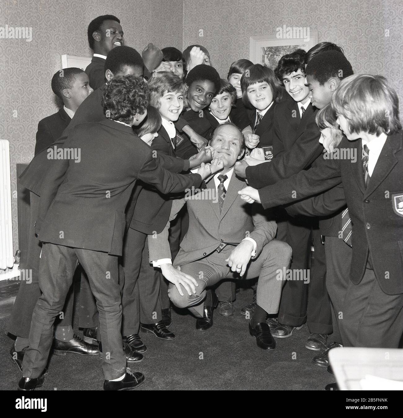 1972, storico, 'Take IT on the Chin'....leggenda della boxe britannica Henry Cooper divertirsi con un gruppo di studenti del South London in visita ad una scuola secondaria della città interna. Foto Stock
