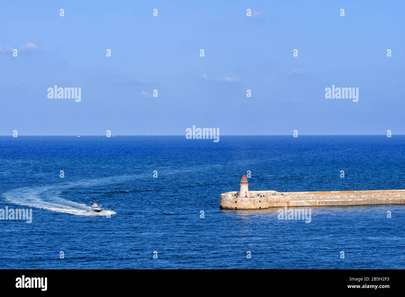 Motoscafo che si avvicina al faro di Ricasoli sulla scogliera di Kalkara, Malta e Grand Harbour nel Mar Mediterraneo Foto Stock