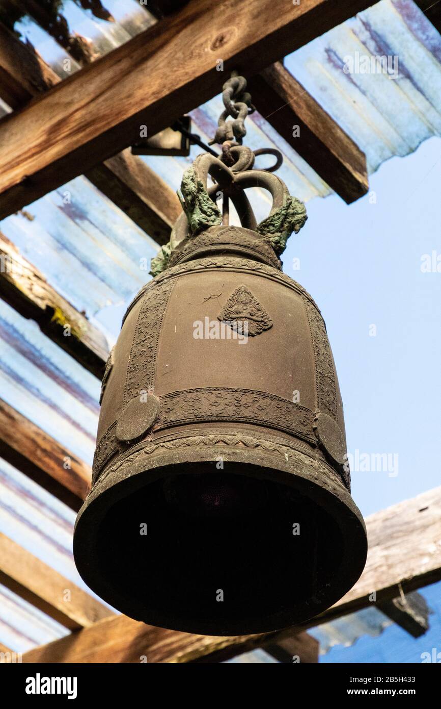 Grande campana tibetana arrugginita pende dal soffitto del gazebo in un giardino zen. Foto Stock