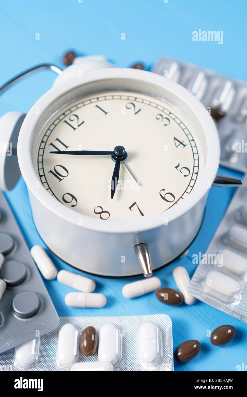 Sveglia analogica con blister di capsule mediche su sfondo di legno azzurro. Concetto contraccettivo Foto Stock
