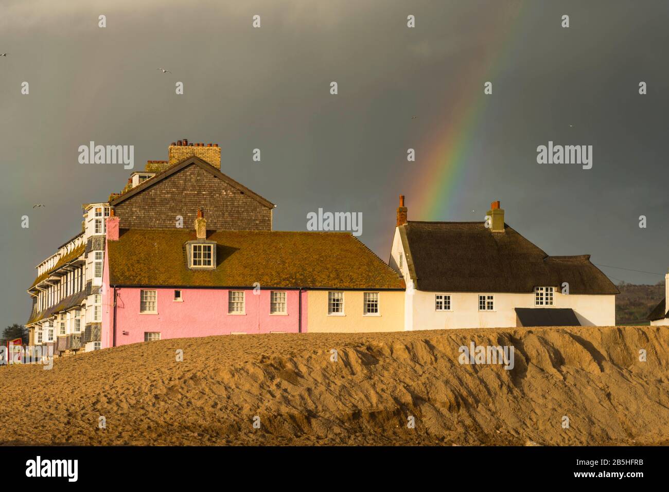 West Bay, Dorset, Regno Unito. 8th marzo 2020. Meteo Regno Unito. Un arcobaleno arcate sopra alcuni cottage fronte mare che sono illuminati dal sole del tardo pomeriggio a West Bay in Dorset come una nuvola di doccia scura passa sopra. Foto Di Credito: Graham Hunt/Alamy Live News Foto Stock