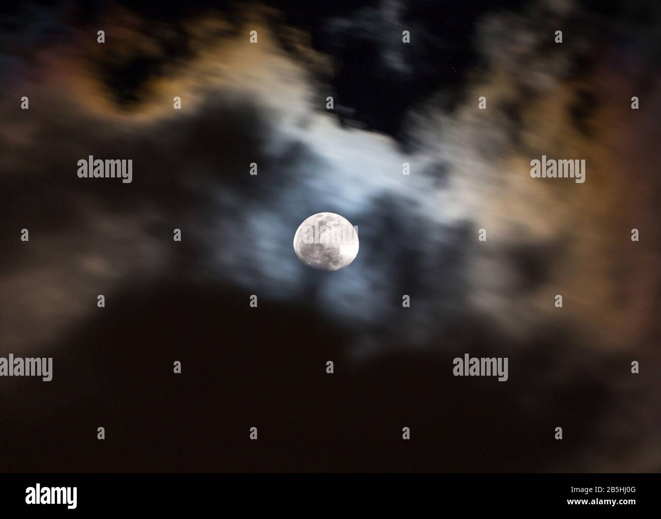 Le nuvole colorate e drammatiche strisciare su una luna piena in un cielo notturno. Foto Stock