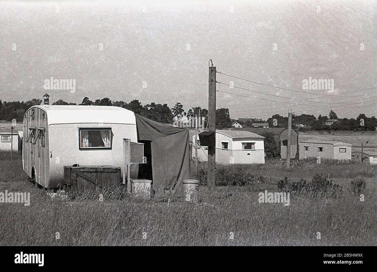 Anni '1950, storici, carovane dell'epoca, possibilmente usate come case mobili permanenti, sedevano in un campo erboso aperto, Inghilterra, Regno Unito, il vicino con una tenda da da sole laterale in tela. Foto Stock