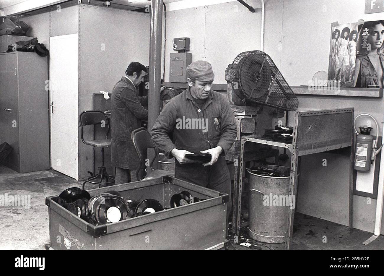 Anni '1970, storico lavoratore maschile in tute con un tronco di rifiuti di plastica, resti di dischi in vinile scartati, USA. La produzione di dischi in vinile è stata una questione sporca e disordinata che coinvolgeva la plastica a base di olio. Foto Stock