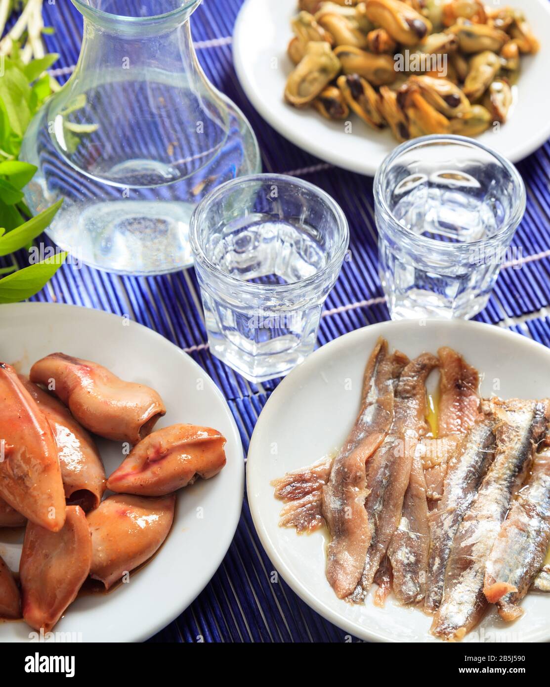Ouzo, raki alcol con meze di pesce su piatti bianchi. Due bicchieri e vari molluschi sani sfondo. Vista ravvicinata, verticale. Foto Stock