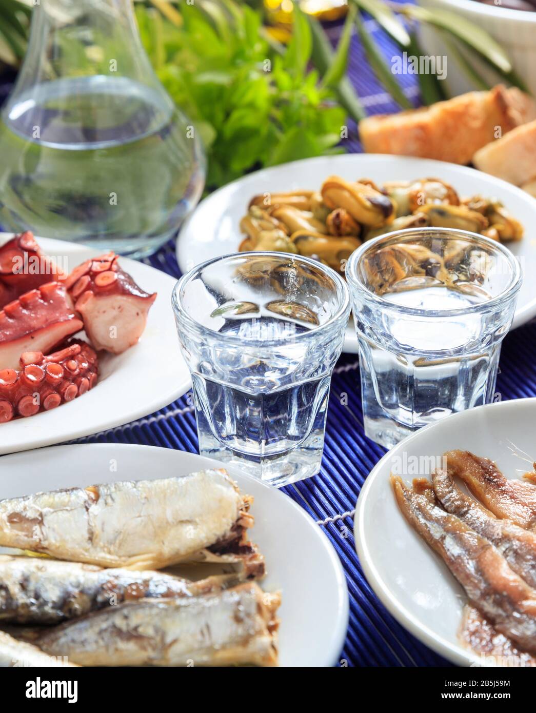 Ouzo, raki alcol con meze di pesce su piatti bianchi. Due bicchieri e vari molluschi sani sfondo. Vista ravvicinata, verticale. Foto Stock