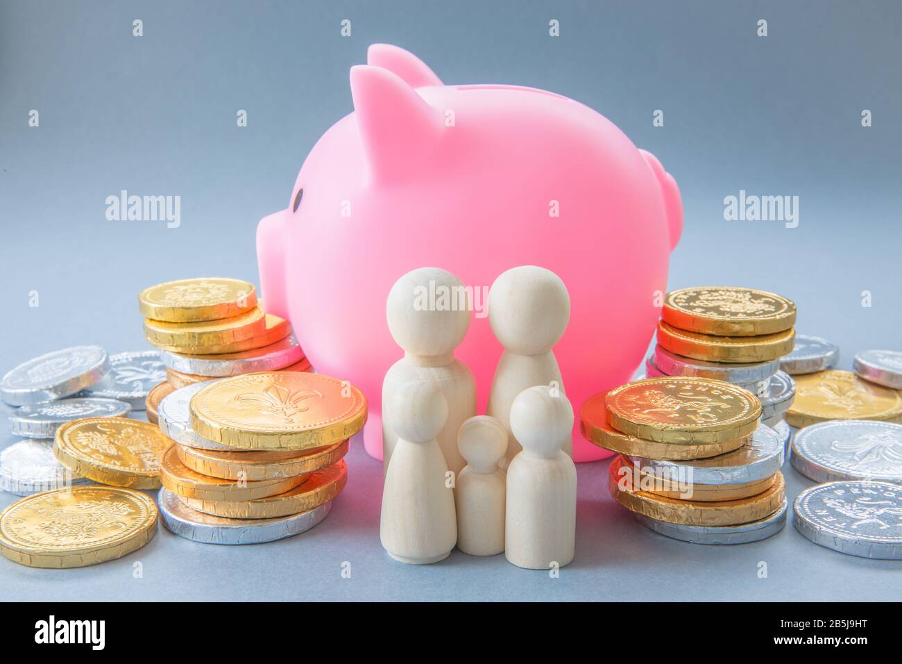 Un'immagine concettuale di una famiglia che sta davanti ad una grande banca rosa di Piggy e circondata da contanti e monete che rappresentano la banca di mamma e papà con c Foto Stock