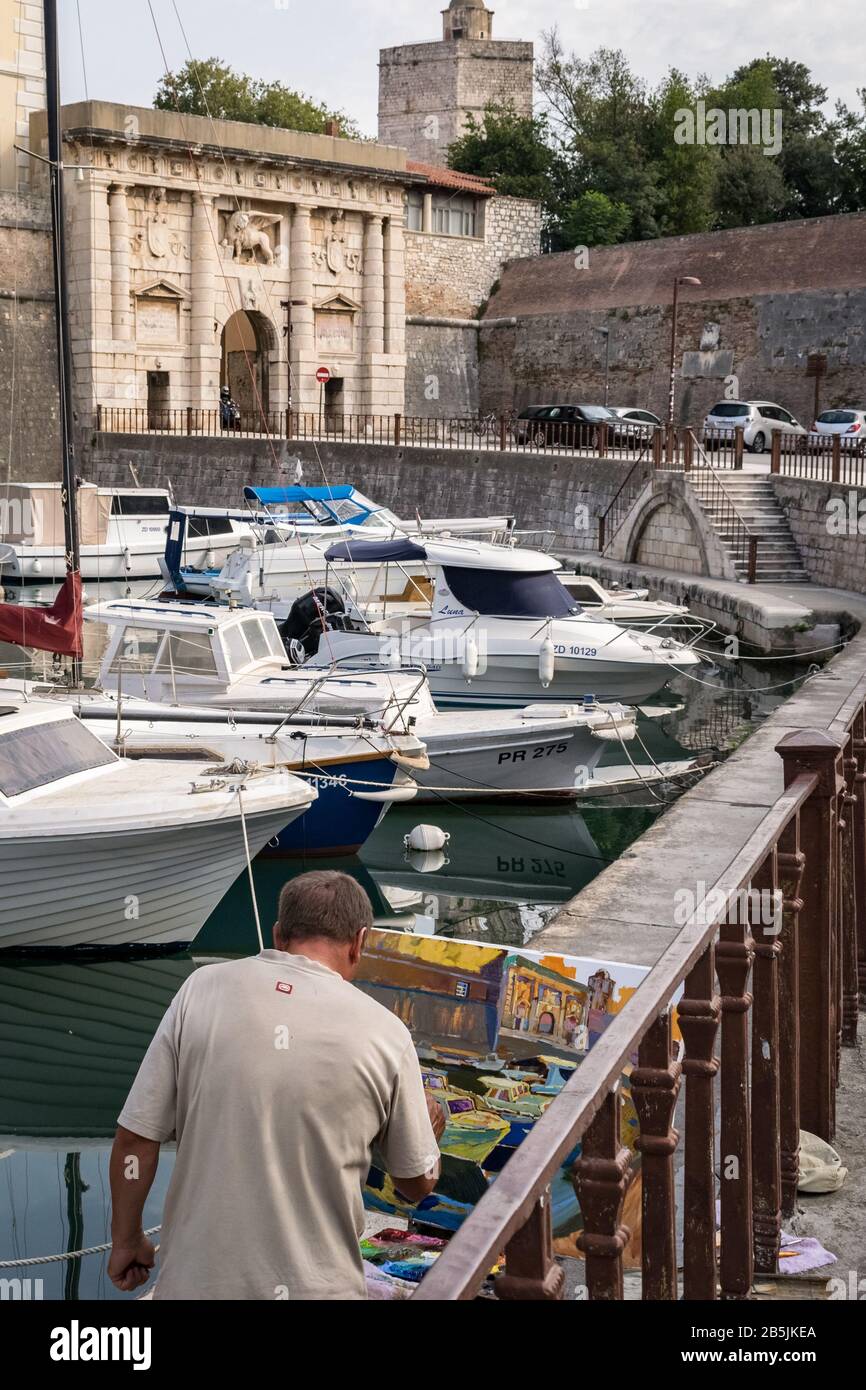 L'uomo che si trova vicino al porto sta dipingendo la porta storica 'Kopnena vrata' (porta Landward) all'entrata della città vecchia di Zara, Croazia. Foto Stock