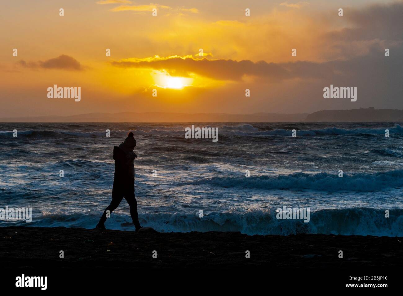 Red Strand, West Cork, Irlanda. 8th Mar, 2020. Una donna solitario cammina lungo la spiaggia di Red Strand mentre il sole inizia a tramontare dopo una giornata di sole e docce. Credito: Andy Gibson/Alamy Live News Foto Stock