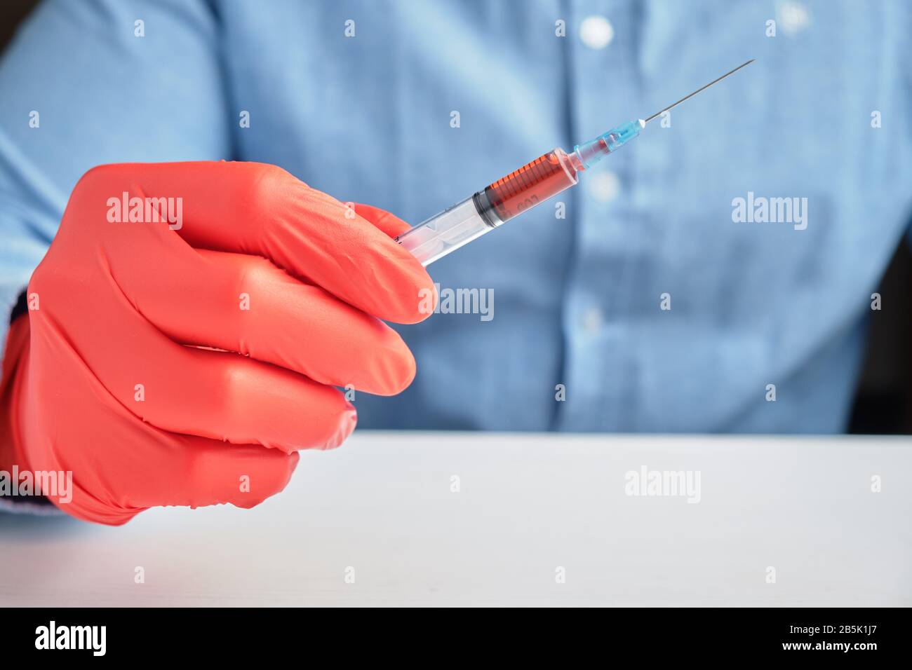 Una mano in guanti rossi contiene una siringa con un vaccino. Primo piano. Foto Stock