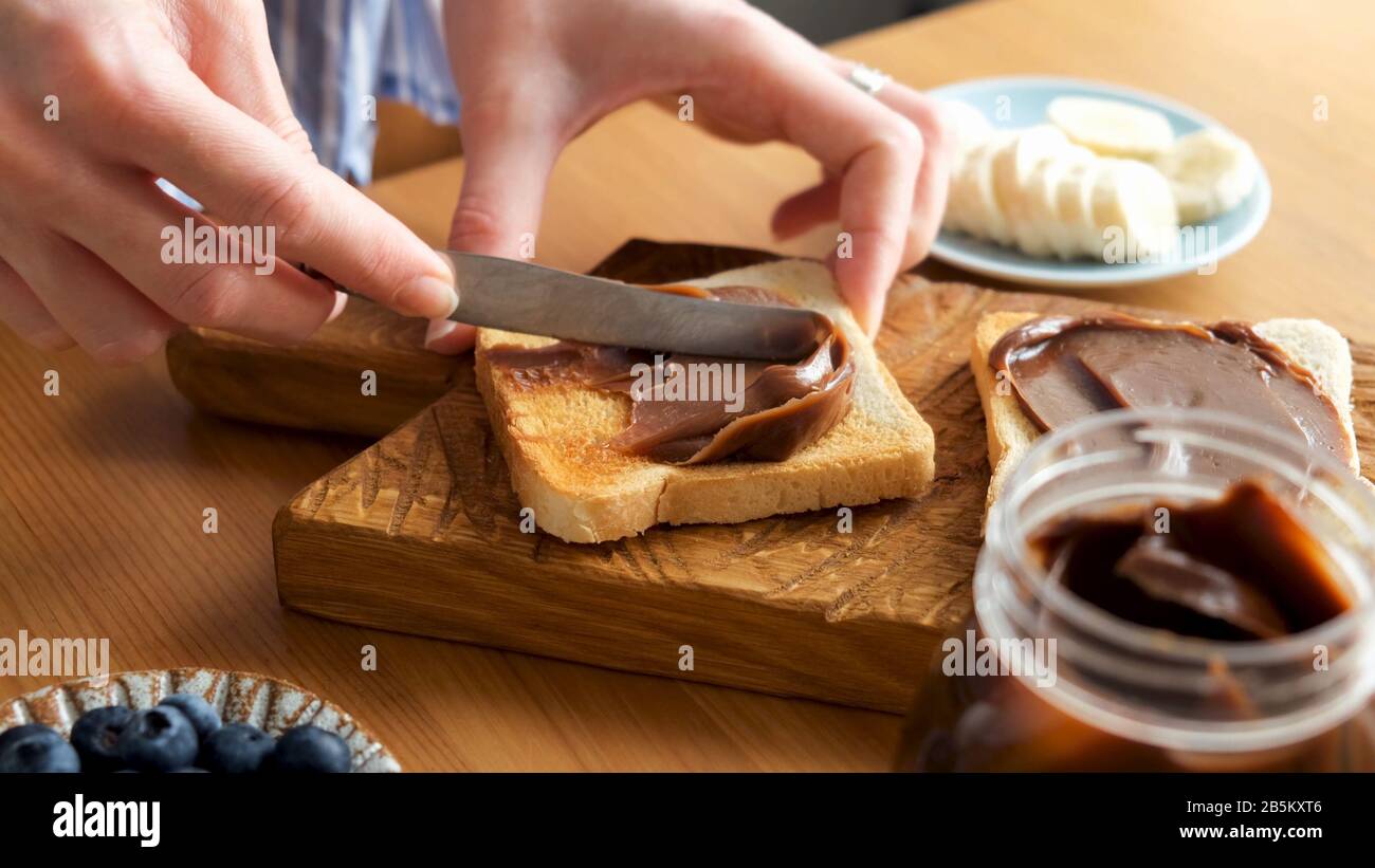 Spalmare il burro di noce di cioccolato sul pane tostato. Mani femminili spalmare il cioccolato sul pane a sandwich. Preparazione del pranzo o della colazione Foto Stock