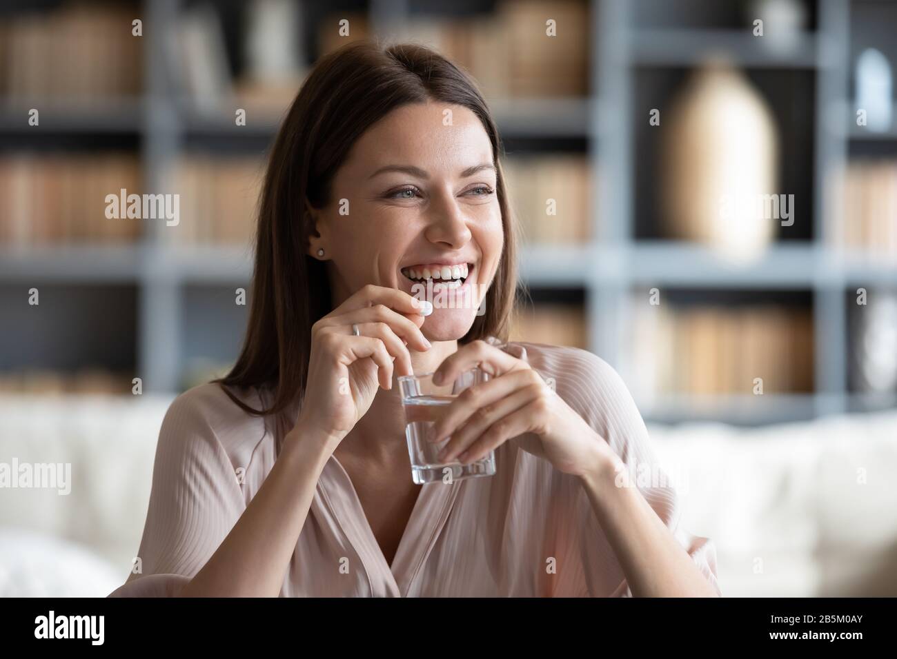 Giovane donna sorridente che tiene la pillola e il bicchiere di acqua pura. Foto Stock