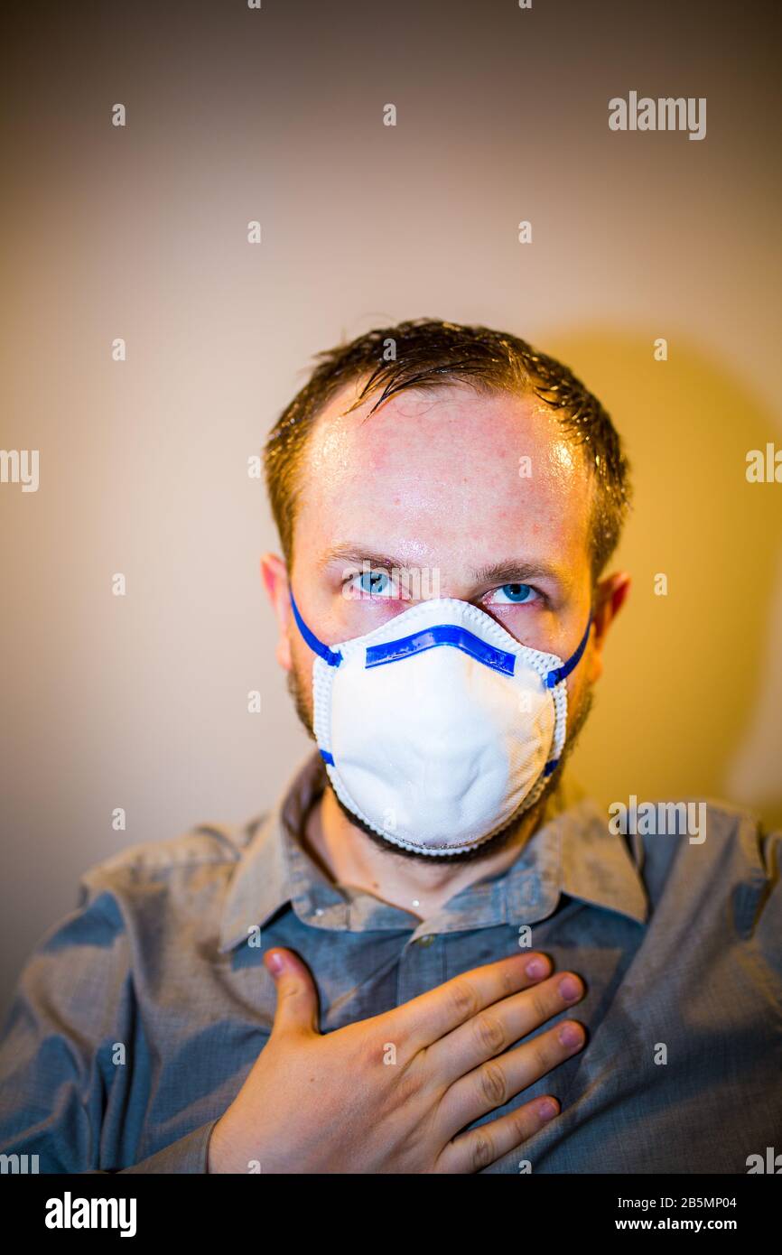 Uomo con Coronavirus reale COVID-19 sintomi di malattia indossa una maschera protettiva Foto Stock