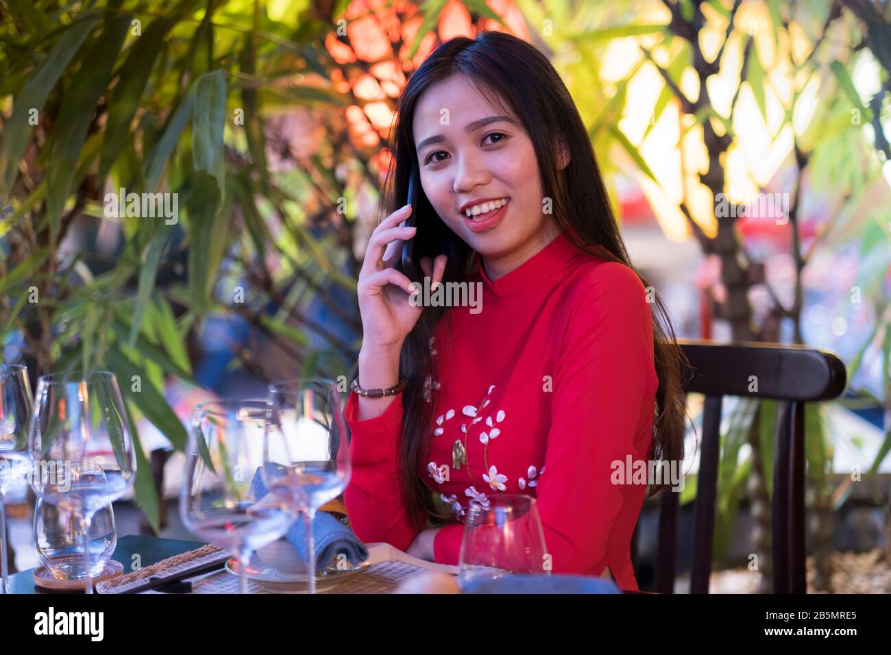 Una giovane donna vietnamita che indossa un tradizionale abito rosso Ao dai utilizzando il suo cellulare Foto Stock
