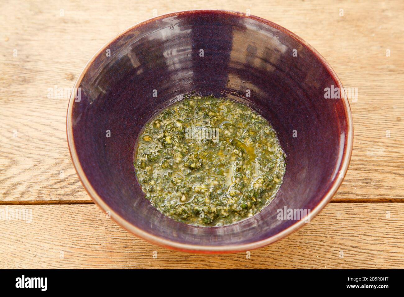 Pesto di basilico in ciotola viola Da Lato sul tavolo di legno Foto Stock