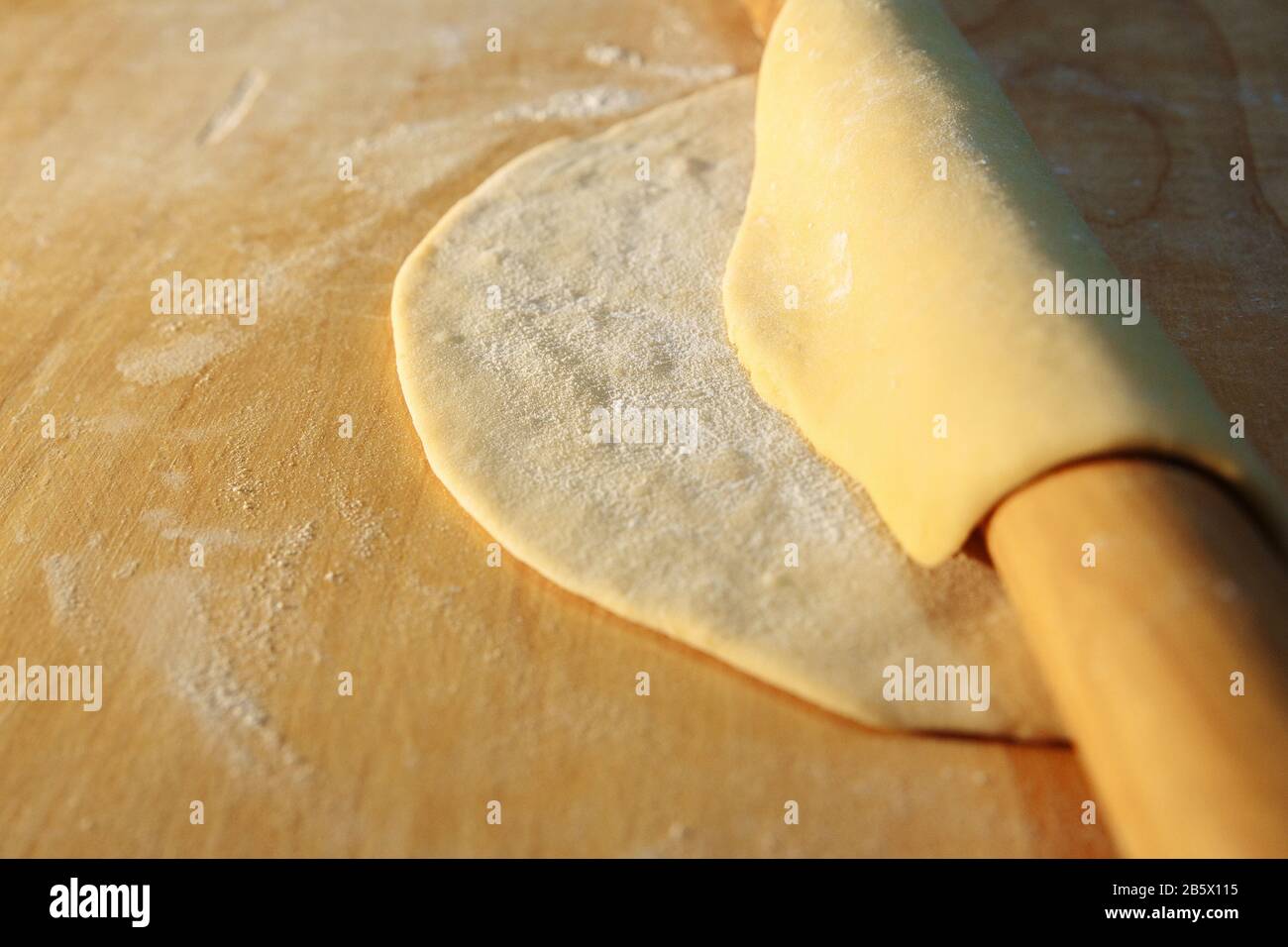 Un pezzo di pasta arrotolato da un perno di laminazione. L'impasto copre un perno di laminazione. Sulla pasta c'è la farina. Foto Stock