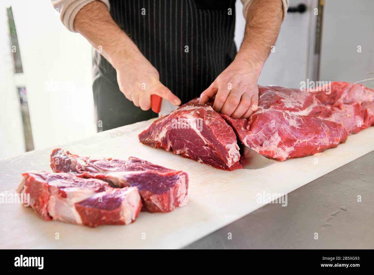 Macellaio o cuoco affettare le bistecche del mandrino, tagliando il pezzo grande di carne fresca. Vista ravvicinata delle mani maschili con un coltello in cucina Foto Stock