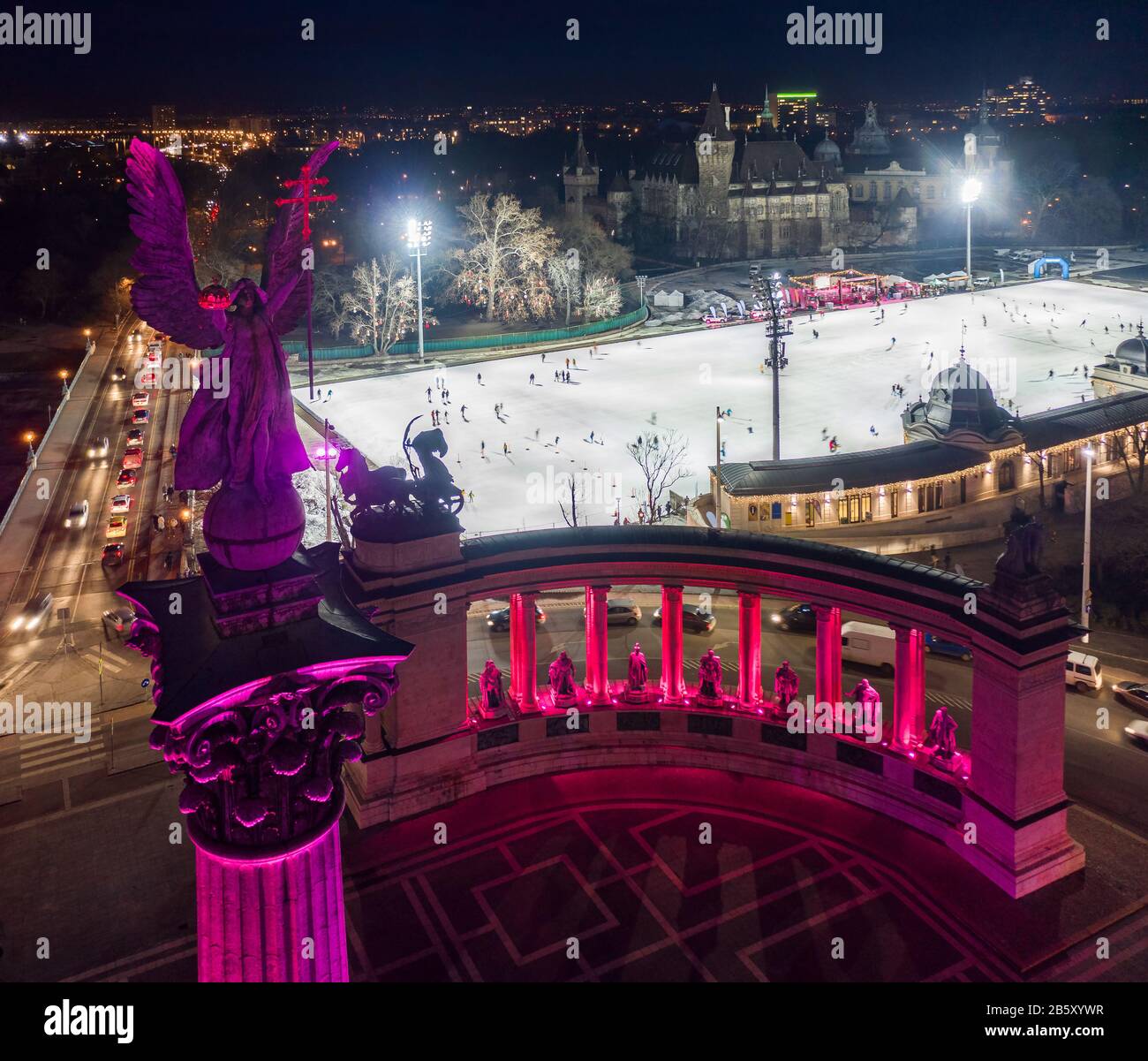 Budapest, Ungheria - veduta aerea serale dell'esclusiva Piazza degli Eroi illuminata di viola e rosa con pista di pattinaggio sul ghiaccio del City Park e Castello Vajdahunyad sullo sfondo Foto Stock