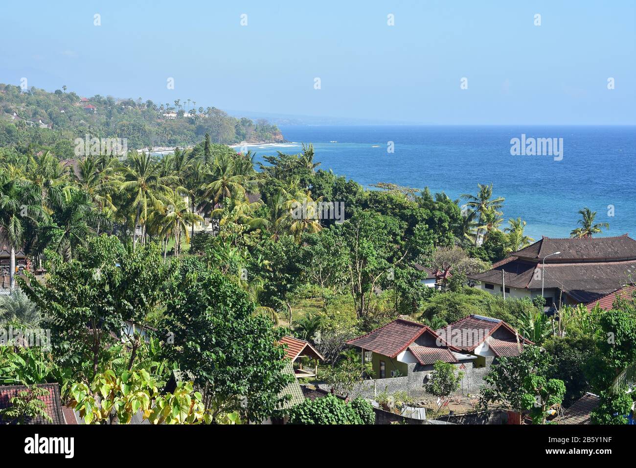 La costa rurale di Bali orientale con case costiere trasformato località di vacanza e fitta vegetazione tropicale. Foto Stock
