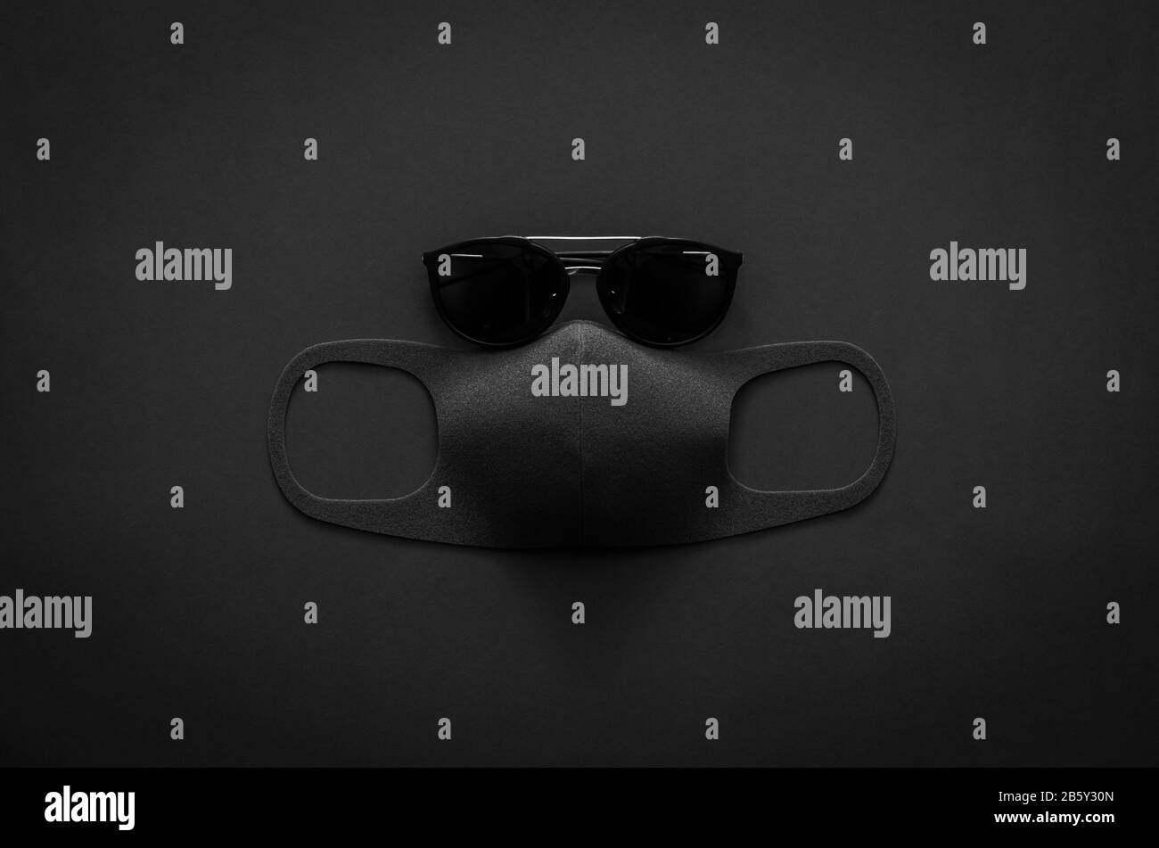 Occhiali da sole e maschera facciale per proteggere il virus su sfondo scuro per un concetto minimalista piatto nero. Foto Stock