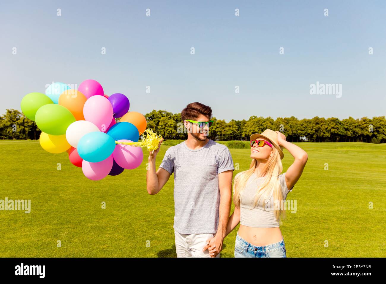 Uomo e donna felici in occhiali con palloncini che tengono le mani Foto Stock