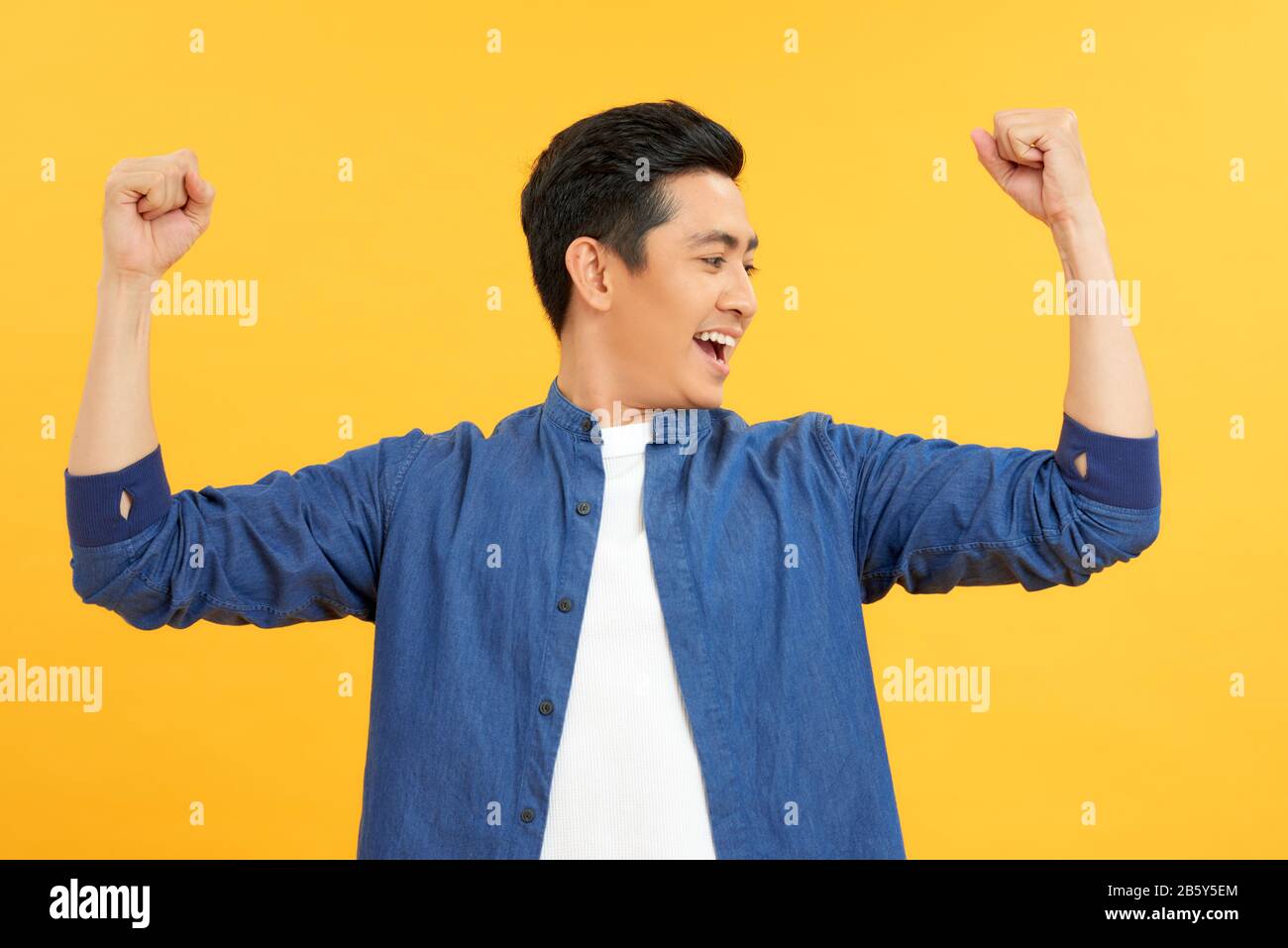 Uomo di successo con le braccia in alto - isolato su uno sfondo giallo Foto Stock