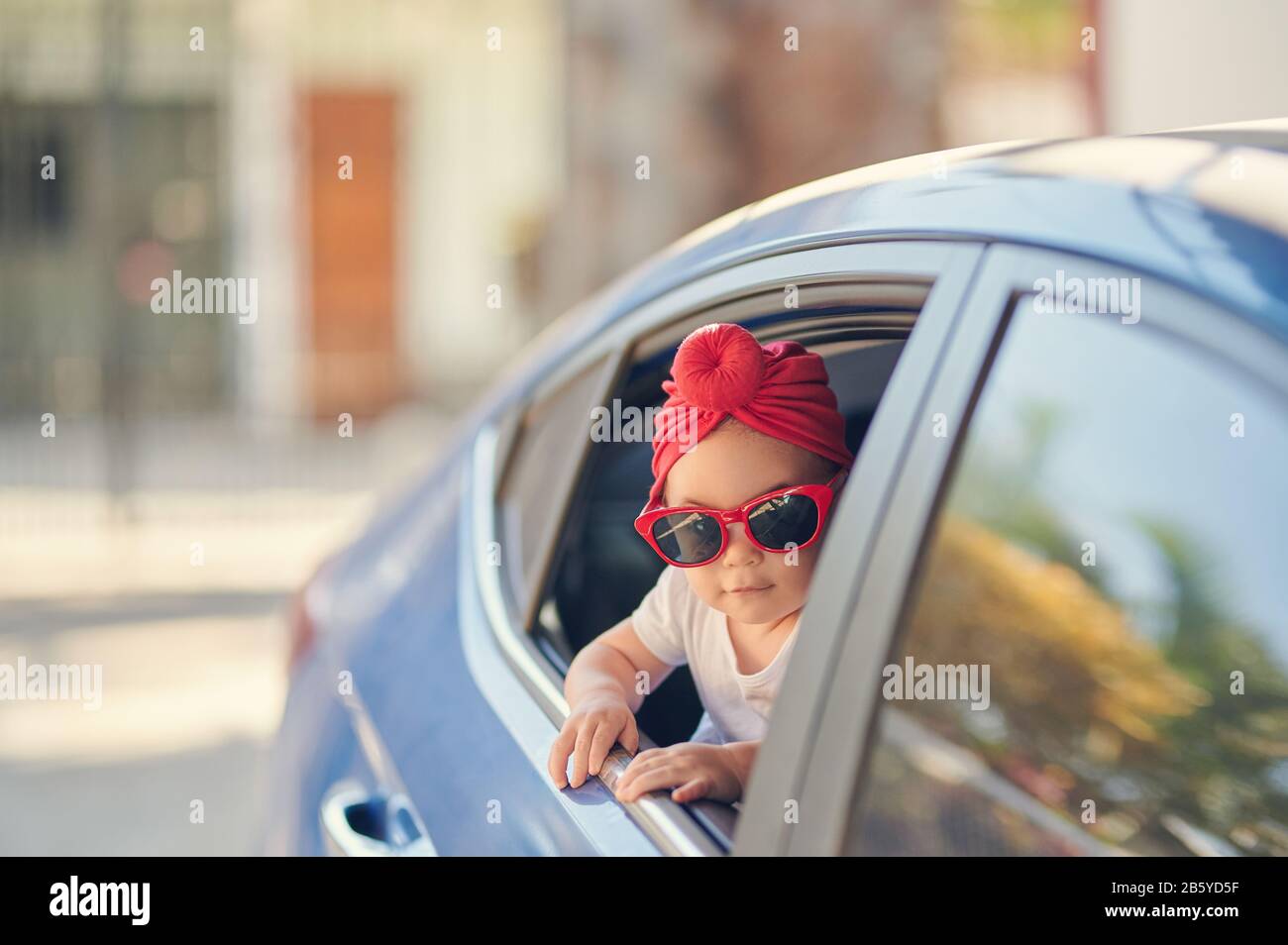 Bambina con occhiali da sole che viaggia in auto e guarda dalla finestra Foto Stock