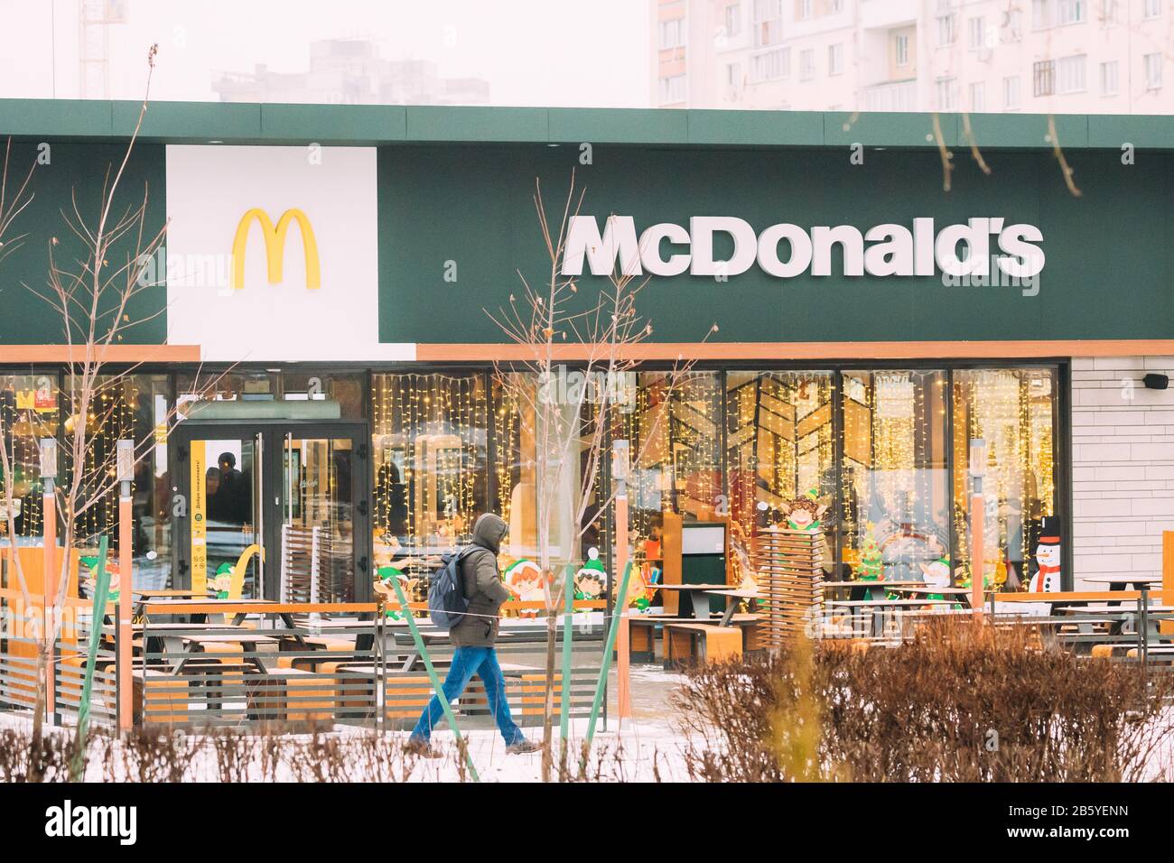 Gomel, Bielorussia - 9 gennaio 2020: Uomo a piedi vicino al moderno edificio del ristorante McDonalds. McDonald's Corporation è la più grande catena di ettari del mondo Foto Stock