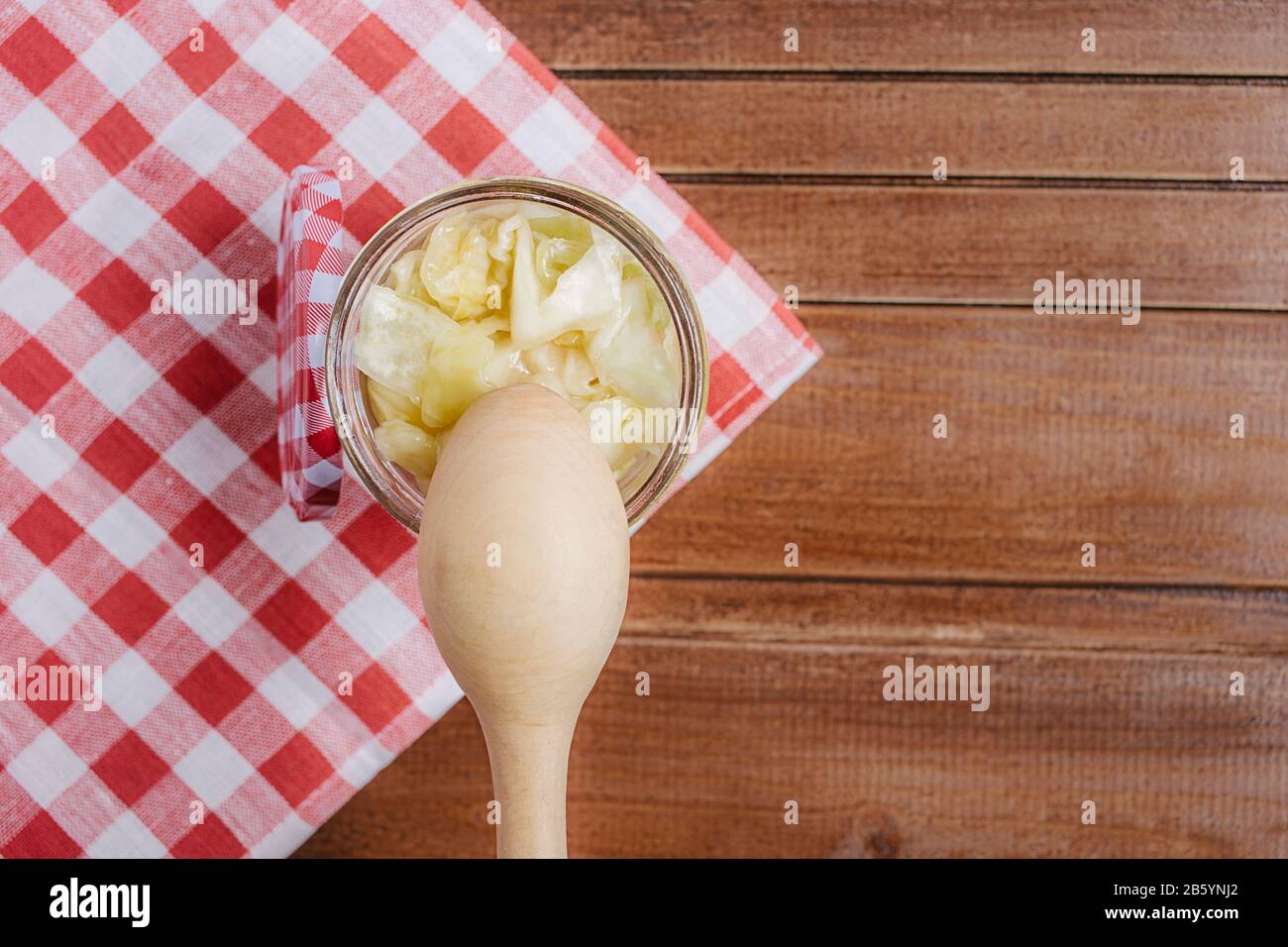 Cavolo fermentato in vaso di vetro con cucchiaio di legno e tovagliolo su fondo di legno. Primo piano. CopySpace. Orientamento orizzontale. Foto Stock