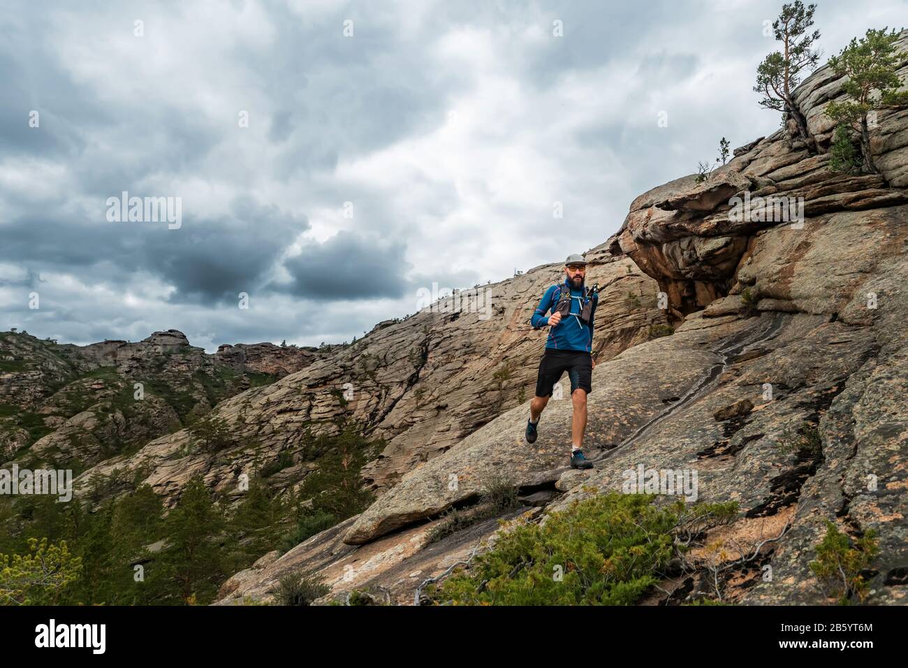 Corridore corre sulle montagne rocciose. Un uomo in Jersey blu e pantaloncini neri sta allenando all'aperto Foto Stock