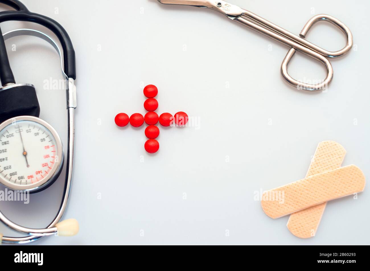 strumento medico isolatad su sfondo bianco, stetoscopio, forbici, cerotto, segno di salute fatto da pillole rosse Foto Stock