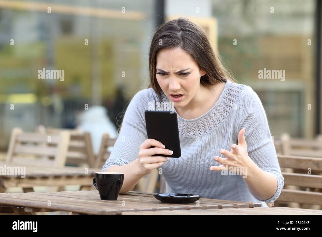 Ragazza arrabbiata che guarda il suo smartphone infastidita su una terrazza ristorante Foto Stock