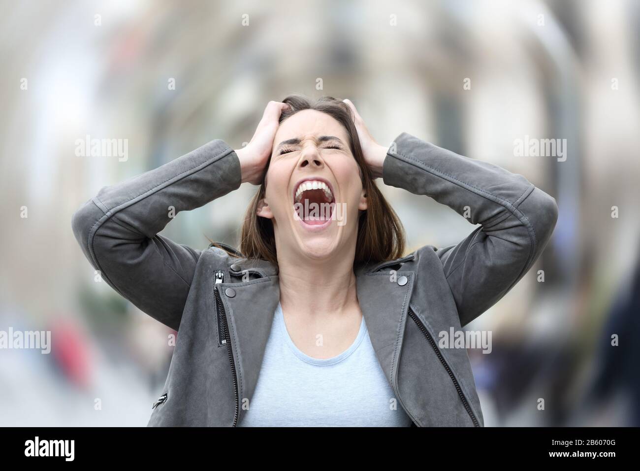 Il ritratto della vista anteriore di una donna stressata che urla l'attacco di ansia di sofferenza disperata afferrando la sua testa sulla strada della città Foto Stock