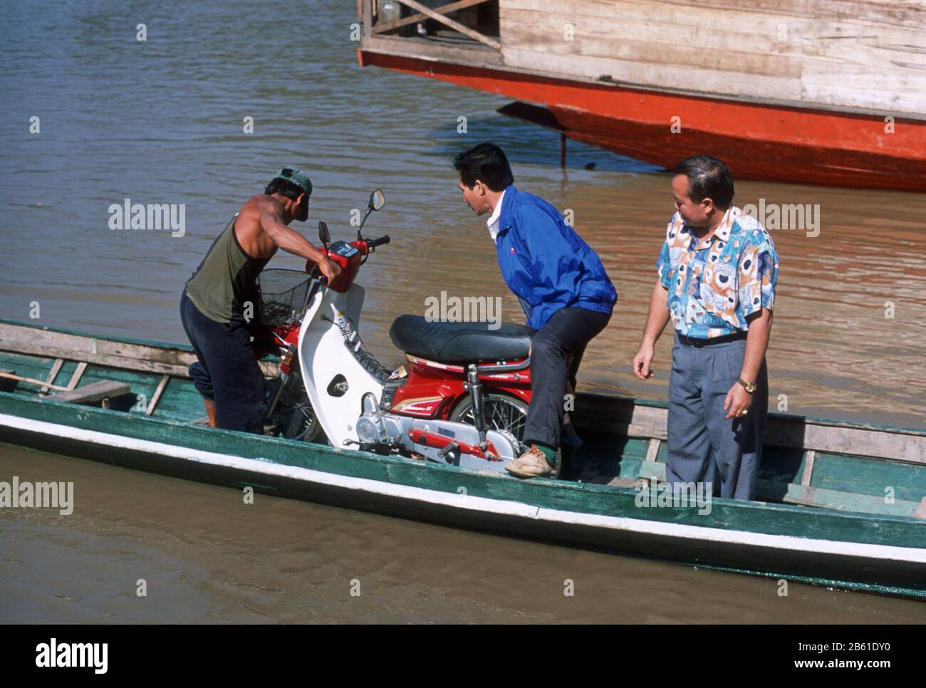 Tre uomini organizzano una moto in una piccola barca per imbarcarla attraverso il fiume Mekong a Luang Prabang, Laos, S.E. Asia. La città di Luang Prabang è patrimonio dell'umanità dell'UNESCO. Foto Stock